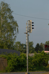 A traffic light mounted on a tall pole surrounded by lush trees in the background, creating a...