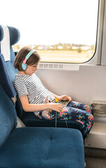 Child with a smartphone and earphones travels by train. Family travelling concept.