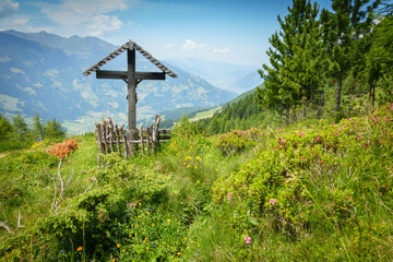 Wegkreuz umrahmt von Alpenrosen mit Blick ins Zillertal