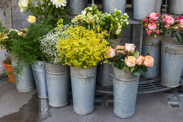 An expansive and colorful outdoor flower shop display features a wide array of blooming flowers and plants in galvanized metal buckets and pots.