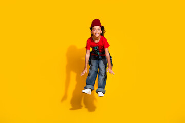 Cheerful young girl wearing red and denim jumps joyfully against a vibrant yellow background showcasing youthful fashion