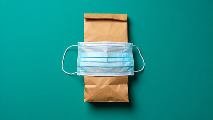 A face mask resting on a brown paper bag against a teal background