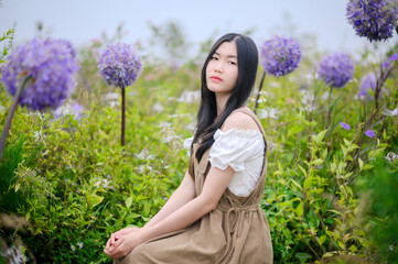 asian woman in a white blouse and brown dress sitting quietly among blooming purple allium flowers...