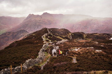 Hiker descending Lingmoor Fell on a rainy day, looking towards the Langdale Pikes, Great Langdale,...