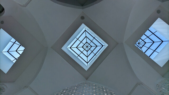 Modern architectural interior with geometric glass ceiling and natural lighting, featuring symmetrical skylight patterns in a white minimalist setting. - Powered by Adobe