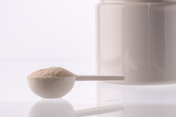 Collagen powder in a measuring spoon and jar on a white background with reflection. A dietary supplement for beauty, health and weight loss.