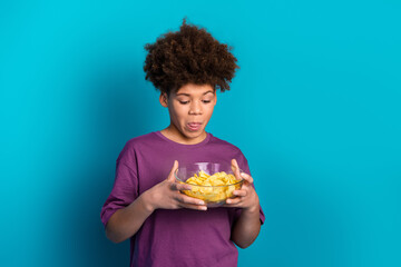 Happy teenage boy enjoying snacks in a bowl against a vibrant blue background, expressing casual...