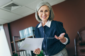 Confident mature professional businesswoman with grey hair presenting confidently in a bright...