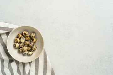 Fresh quail eggs in bowl on striped cloth with light background for culinary use
