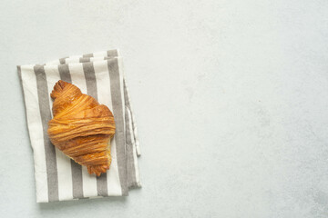 Golden croissant on striped napkin with minimalist gray background
