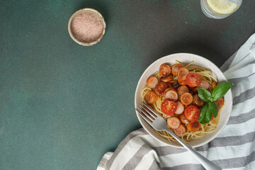 Spaghetti with sausages and cherry tomatoes garnished with basil on rustic table setting