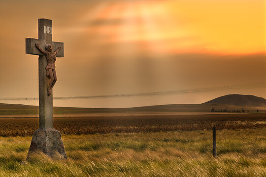 Large crucifix stands in field at sunset with power lines