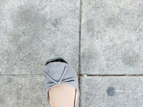 Woman's grey shoe on concrete sidewalk tile