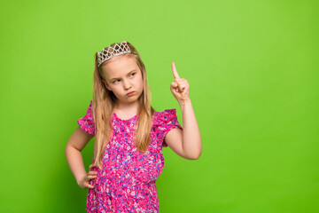 Cute Little girl in a decorative hair accessory shows a playful gesture against a green background.