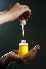 Mockup of glass bottle with dropper cap in female hands. Amber container with cosmetic product,...