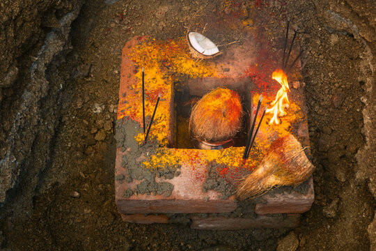 A traditional South Indian Bhoomi Puja setup featuring a lit camphor fire, coconut, turmeric, red powder (kumkum), and ceremonial bricks. This sacred ritual is performed to seek blessings from Mother 
