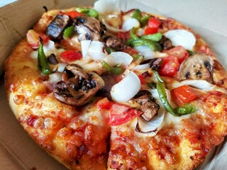 Tasty fully baked pizza with toppings of white onion, tomatoes, green bell pepper and mushrooms undboxed order delivering in cardboard box packaging.
