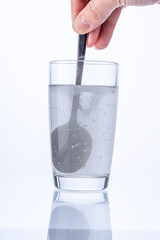 Collagen or medicinal powder is stirred with a spoon in a glass of water on a white background.