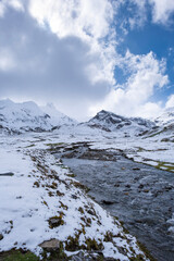 Snowy mountain landscape with a clear stream flowing through a valley under a partly cloudy sky