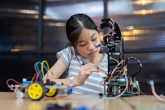 Girl while working Assembly, installation or repair programming robotic arm. Environment features  modern classroom with technology and education tool, enhancing creativity and learning.