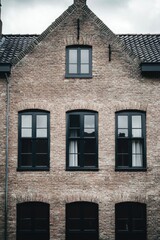 Fototapeta premium Brick townhouse facade showcasing large windows and dark trim under a cloudy sky in a quaint neighborhood during the late afternoon