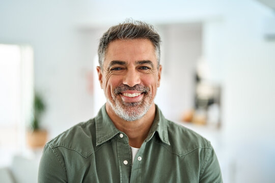 Smiling older mature 50 years old handsome man looking at camera posing in modern house living room. Happy confident middle aged senior man standing at home. Close up face portrait.