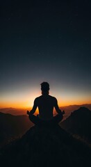 Silhouette of male meditating at sunset on mountain peak with starry sky