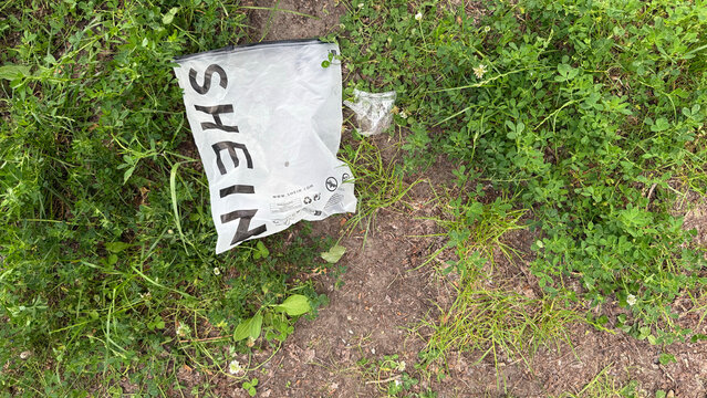 Warsaw, Poland - June 19, 2025: SHEIN plastic bag discarded on grassy ground in a natural outdoor setting