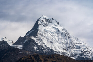 A breathtaking view of the snow-capped peak of Annapurna South when the clouds softly hug the mountains in great Himalayas in Nepal.