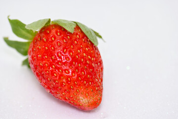 Freshly picked strawberry lying on a clean surface with bright red color and green leaf