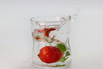 Splashing strawberry in clear water within a glass vessel captured in indoor light