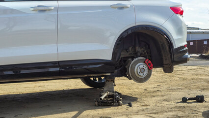 A white car with a flat tire is being lifted by a jack. The tire is being replaced with a spare tire