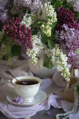 A bouquet of lilacs on the table and a cup of tea.