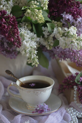 A bouquet of lilacs on the table and a cup of tea.