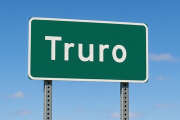 Truro town entry sign displayed on a green road sign with a bright blue sky in the background, suggesting travel.
