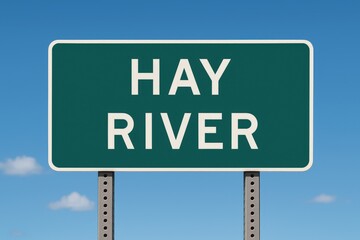 Green road sign displaying "Hay River" against a bright blue sky, representing city entrance, travel direction, or Northwest Territories location.