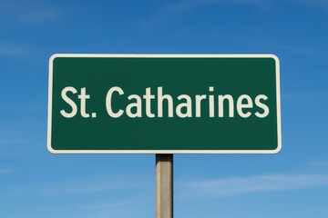 Green road sign displaying "St. Catharines" beneath a clear blue sky, indicating city entrance, travel direction, or Ontario location.