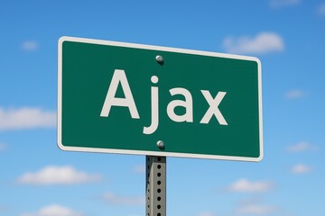 Green road sign showing "Ajax" against a clear blue sky with scattered clouds, indicating city entrance or travel direction.