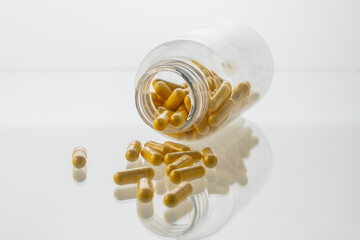 A jar with pills inside lies on a white background with reflection. Hyaluronic acid, collagen,...