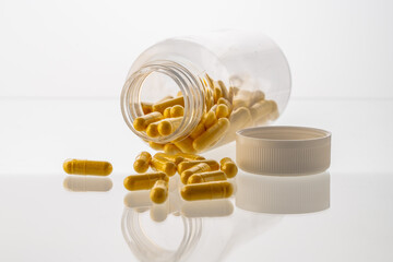 A jar with pills inside lies on a white background with reflection. Hyaluronic acid, collagen,...