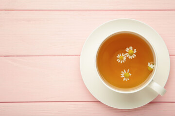 Aromatic herbal tea in white cup and chamomiles on pink background. Space for text