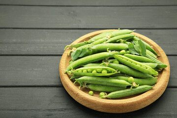 Fresh green peas in wooden bowl with pods and leaves on black wooden background, healthy green vegetable or legume