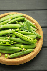 Fresh green peas in wooden bowl with pods and leaves on black wooden background. Vertical photo