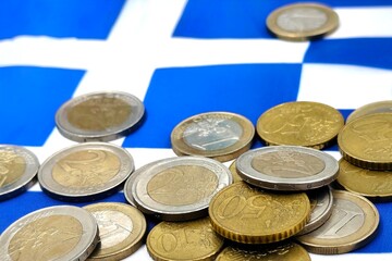 Photo of euro coins scattered over the Greek national flag, symbolizing Greece’s economy, financial matters, and the broader European Union economic crisis.