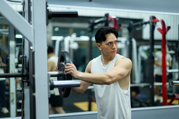 Fototapeta premium Young sportsman adding weights to barbell, focused on strength training in gym