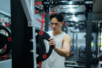 Young sportsman adding weights on barbell in gym