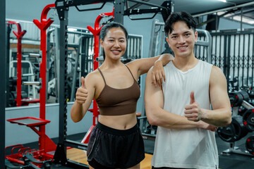 Sporty asian couple showing thumbs up while working out in gym