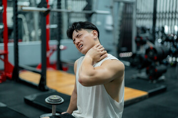 Asian athlete suffering neck pain after weightlifting training in gym
