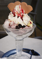 Ice cream with cherry syrup and waffle in glass bowl on dark background