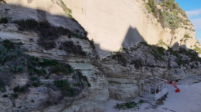 A historic church perched  of Santuario di Santa Maria dell'Isola di Tropeaon a cliff overlooking the ocean, surrounded by lush greenery and a clear blue sky.